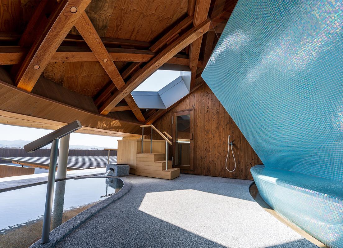 〈天色の湯〉の露天風呂と外気浴スペース。天井の木屋根や天窓に施された六角形のモチーフが印象的。