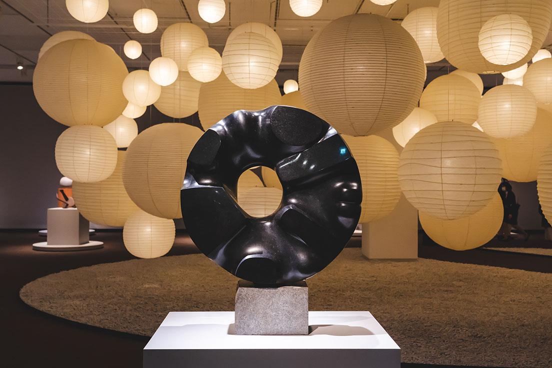 《黒い太陽》（1967−69年、国立国際美術館）の後ろには、イサム・ノグチがデザインした150灯の「あかり」が生きているようにゆっくりと点滅する。　(c)2021 The Isamu Noguchi Foundation and Garden Museum / ARS, NY / JASPAR, Tokyo, E3713