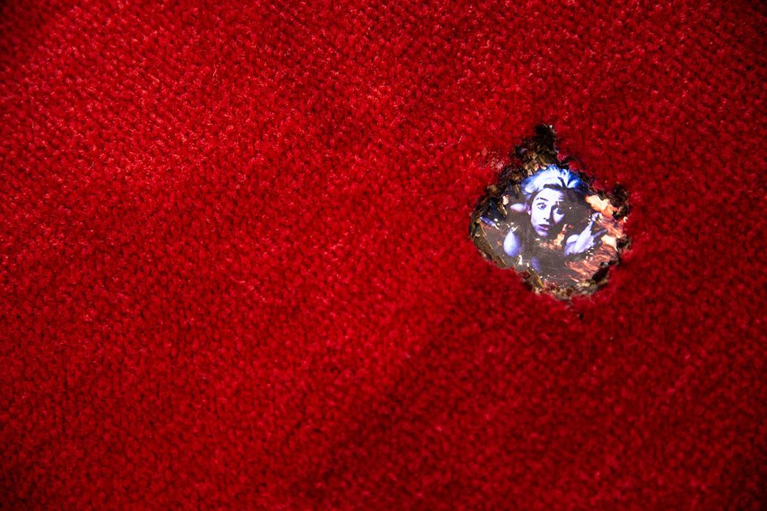 《溶岩の坩堝でわれを忘れて》（1994年）。ロビーの床カーペットに開いた2〜3センチ程度の穴から映像を見る、という作品。大変な状況なのだけれど、ユーモアが漂う。