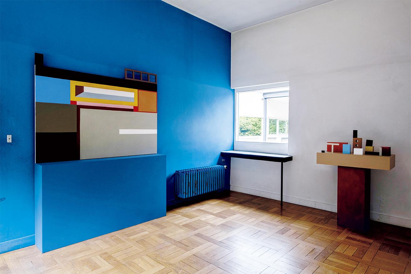 夫妻の私室のインスタレーション。ル・コルビュジエによるブルーの壁と呼応する絵画（左）と日用品を連想させる複合オブジェを乗せた台（右）。