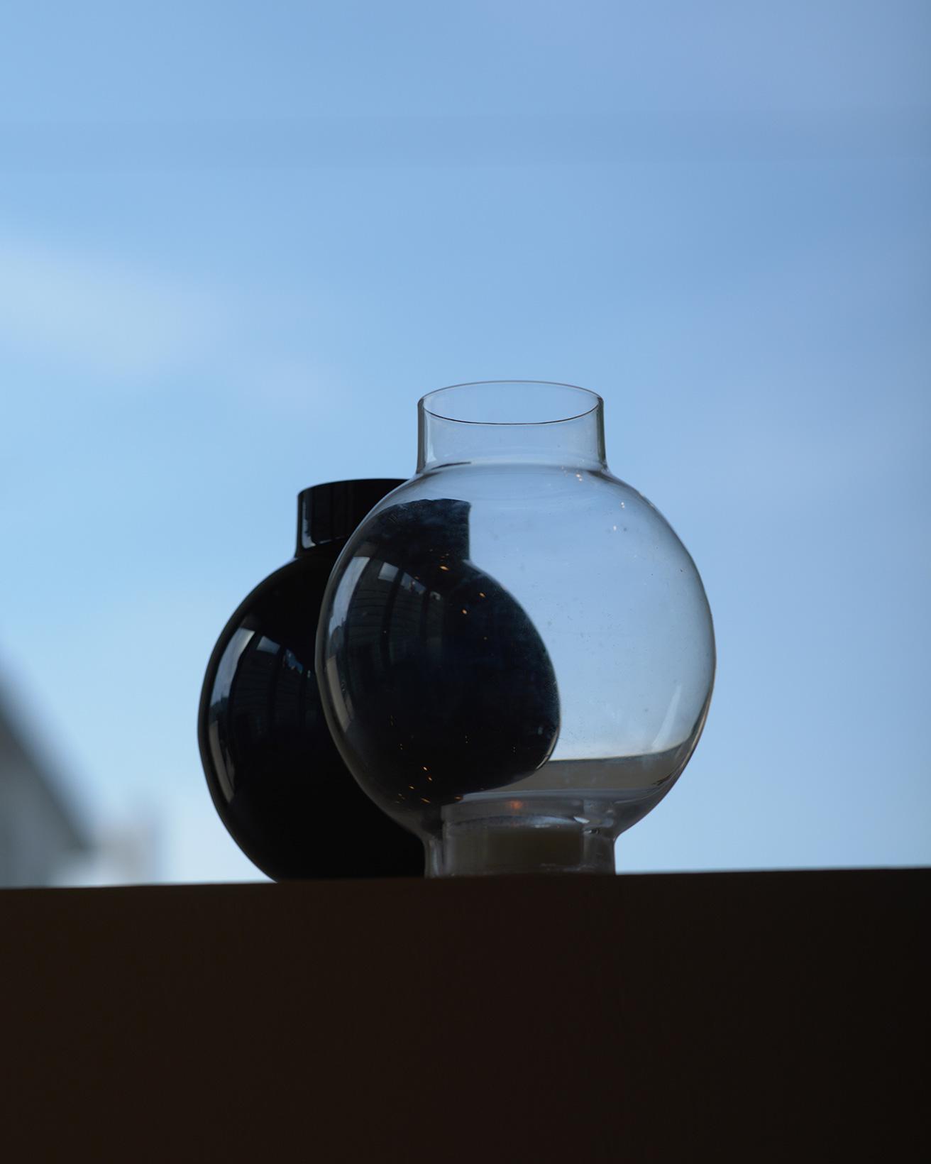 スウェーデンのスモーランド地方で1897年から製造を続けるメーカーによる、ハンドメイドのガラスベース。ガラス作家のカリーナ・セス・アンダーソンは、上下の直線部分と膨らみで豊かなプロポーションを作り出して、まるで提灯のような形に。吹きガラスならではの輪郭の揺らぎがあり、ブラックも光が当たると透けるクリアなガラス。〈スクルーフ〉の《トーキョー ベース L》［H15×φ12cm］クリア5,720円、ブラック6,600円（共にディエチ TEL 06 6882 7828）