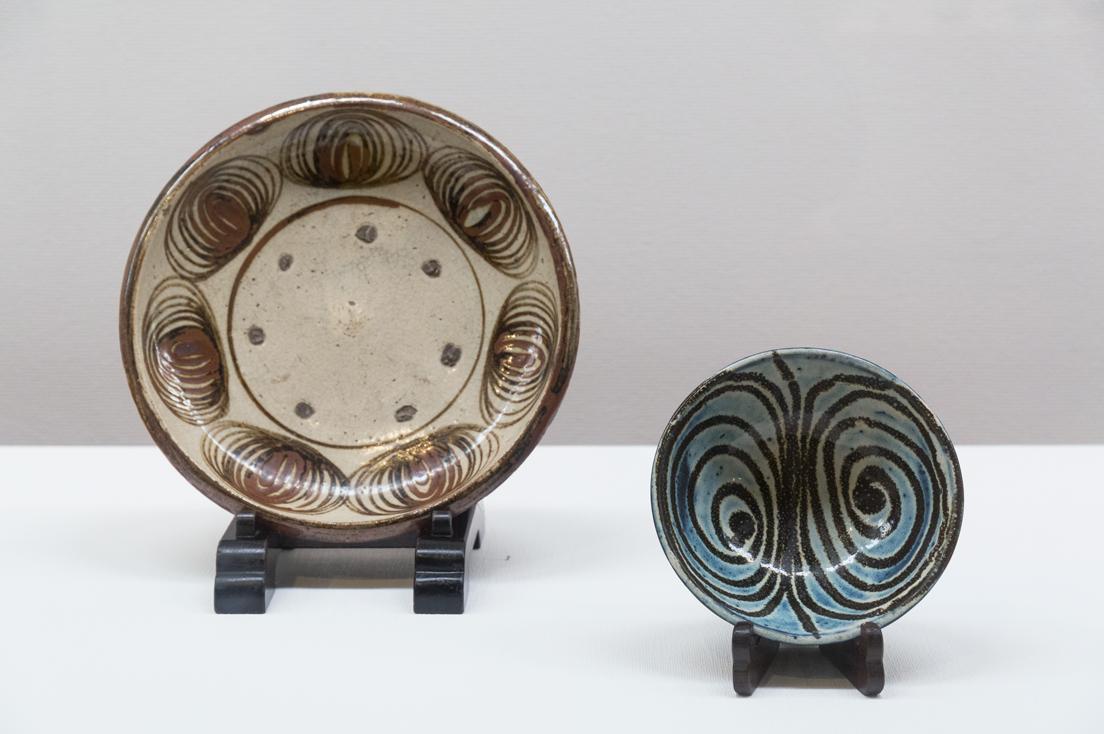 江戸時代の瀬戸（愛知県）の《馬の目皿》（左）と、河井寬次郎による《海鼠釉渦文皿》（右、1925年頃）。河井の作品は、古い民藝の器からインスピレーションを得ていたことを窺わせる。いずれも日本民藝館。