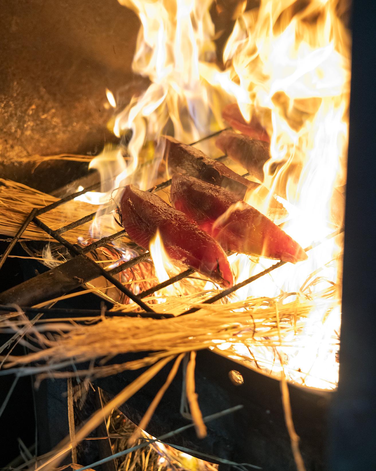 この火力！　たたきの味を左右するカツオの藁焼きは4代目、田中社長が担当する。強火で一気に表面を焦がすように焼くのが田中鮮魚店流。また、藁のスモークしたような香りをまとわせるのもポイント。