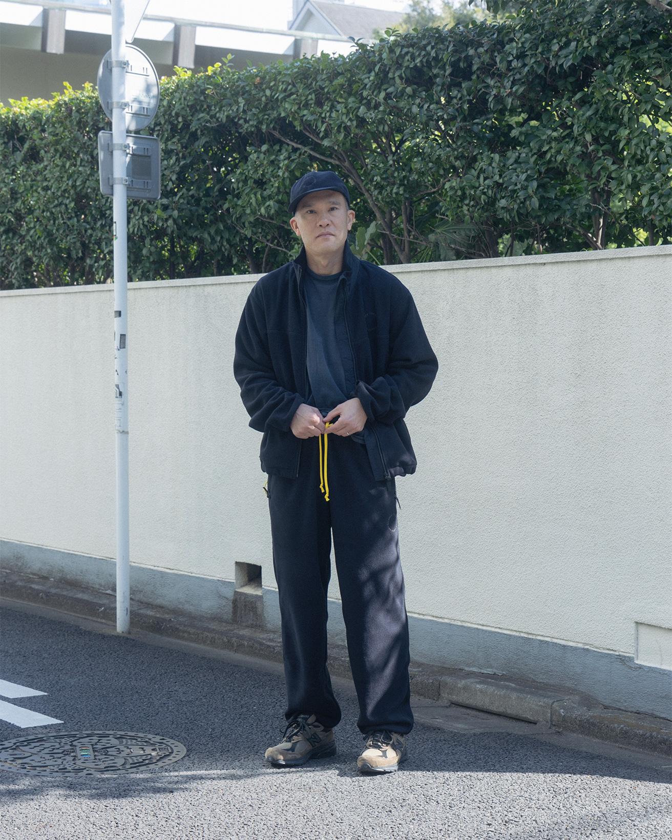 現代美術作家の加賀美健が着るのは〈Uni-ssentials by TDS〉のセットアップ。ワンポイントに黄色を使う。