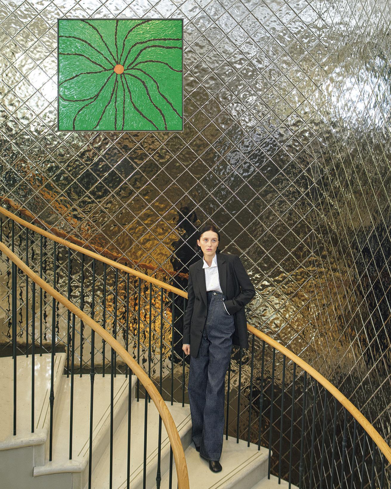 ロエベの世界観を象徴する曲線を描くように続く階段。〈カサロエベ〉の店舗において、階段のプランニングは最初に構想される重要な要素。手すりはアーツ＆クラフツ運動、曲線的なフォルムはジョージアン様式の建築が着想源に。壁面の絵画は、リチャード・ホーキンスの作品。ジャケット265,100円、シャツ148,500円、デニムパンツ137,500円※参考価格、ブーツ187,000円（以上ロエベ／ロエベ ジャパン クライアントサービス）。