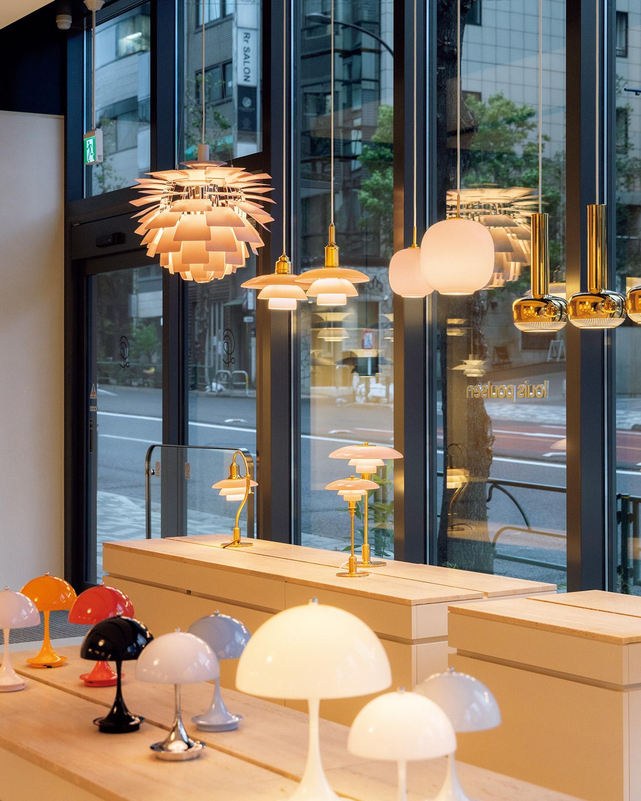 外苑西通りと青山通りが交差する角地に、2023年11月10日にオープンした〈ルイスポールセン東京ストア〉の店舗1階部分。穏やかで上質な表情を持つトラバーチン製天板のショーケースの上に、さまざまなコレクションが並ぶ。開放的な窓辺に並べられた照明の美しい光が、街角を照らしている。
