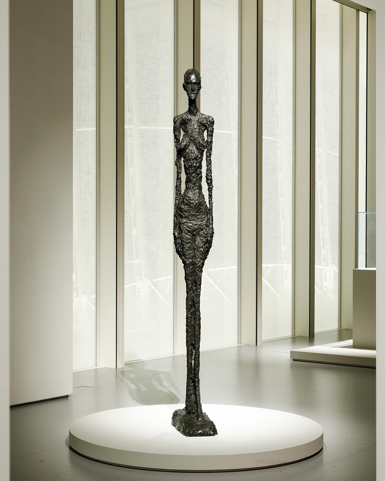 《大きな女性立像Ⅱ》（1960年）。1960年代に制作された一連の《大きな女性立像》は、女性の裸体を扱ったジャコメッティ最後の作品。暗褐色の緑青を施したブロンズ。前傾した台座により、彫刻が上に向かう印象が強調され、削ぎ落とされたようなシルエットと、肥大化した足部によって空間との新たな関係性が生み出されている。