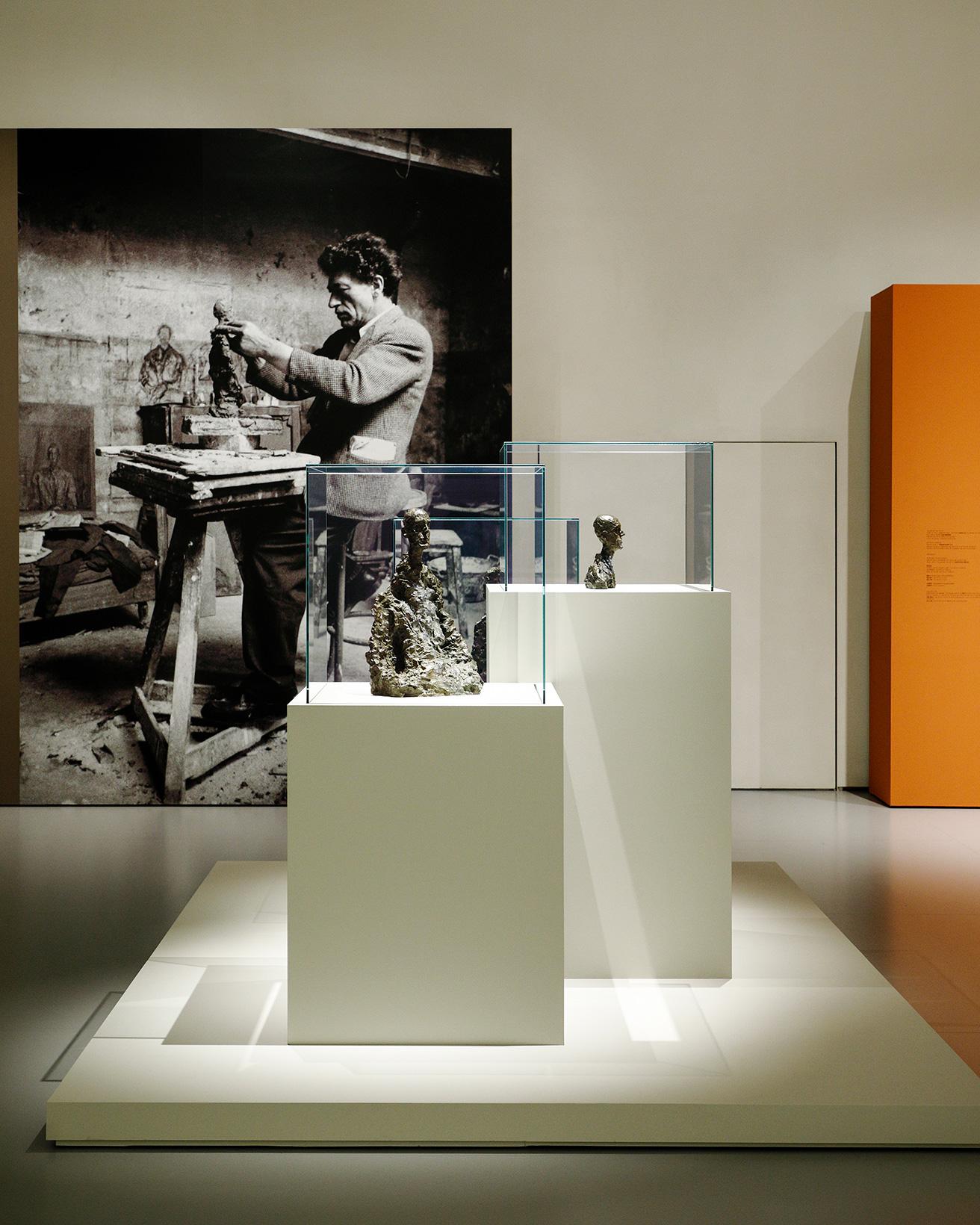 奥に見えるのは1954年に撮影された、パリのアトリエにいるアルベルト・ジャコメッティ。展示された彫刻作品は、まるでアトリエから抜け出してきたようにも見える。