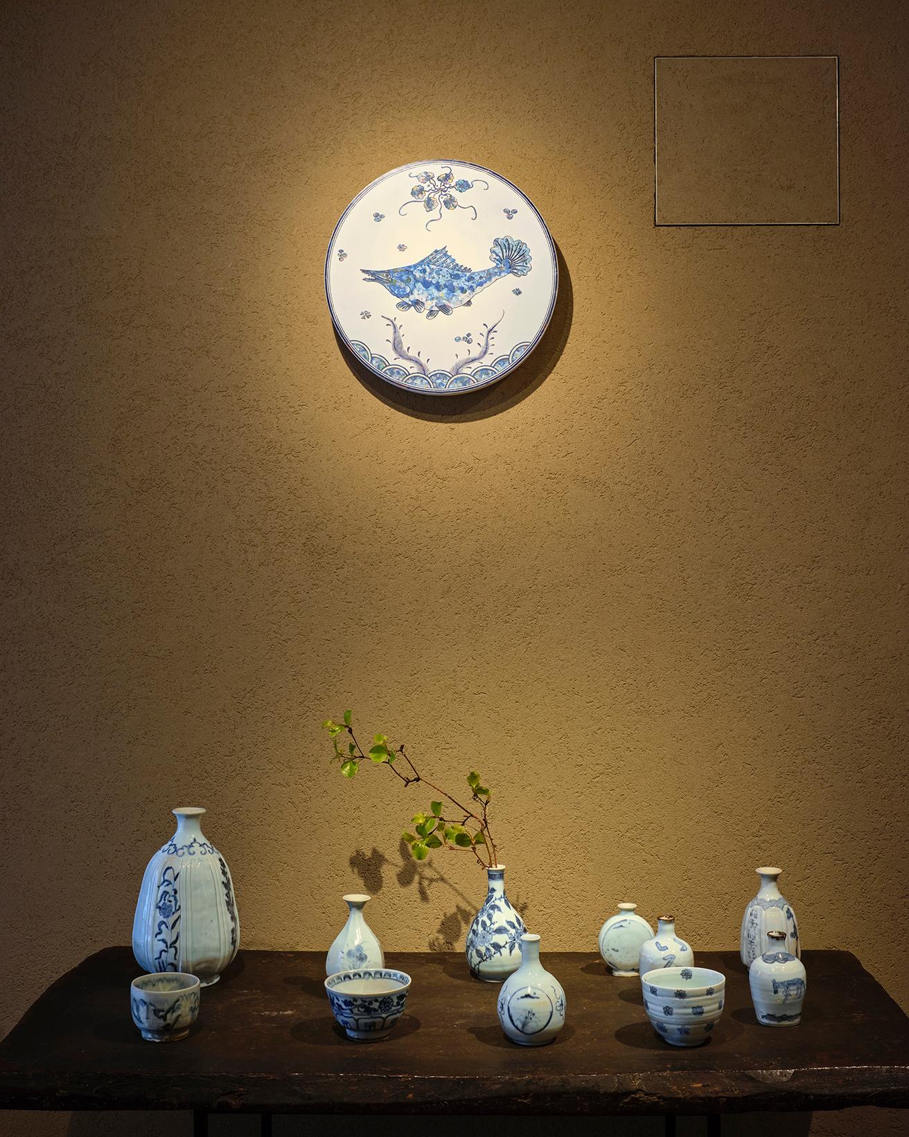 村上隆作品《ケツギョ 水中鱖魚圓平皿 古染付 賛》2023 φ400×50mm。徳利や小鉢、湯呑みなど、さまざまな陶芸作品が並ぶ。 