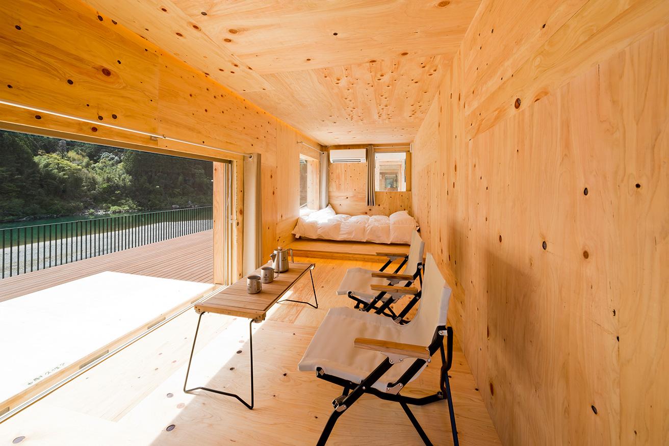 モバイルハウス〈住箱-JYUBAKO-〉は室内外すべて木製で、ベッドとテーブル、椅子のミニマルなスペック。大窓から景色が一望できるのが特徴。