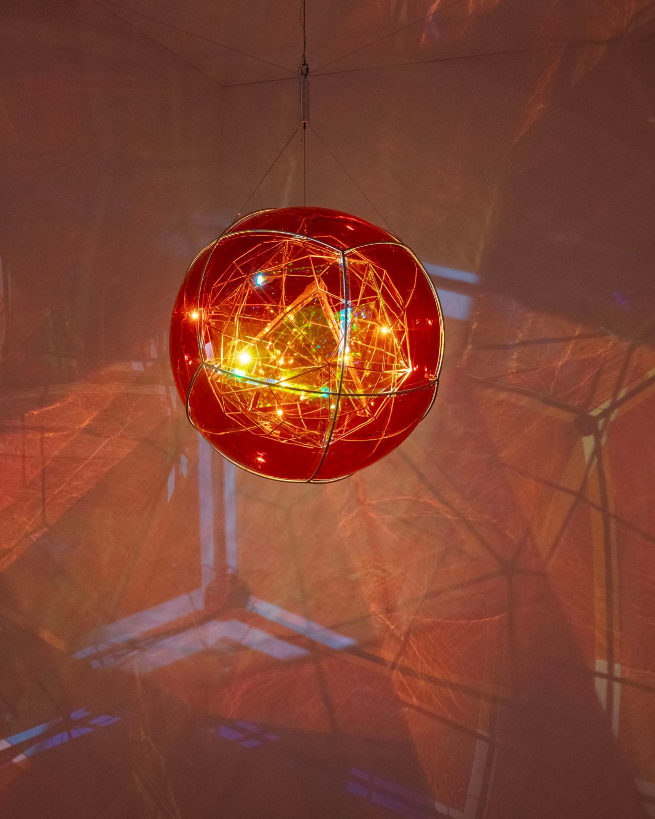 《蛍の生物圏（マグマの流星）》。同心円状に配置された３つの多面体。LEDライトと部分的に反射したり一部の光を透過させるガラス、モーターによって壁に複雑な影を作る。