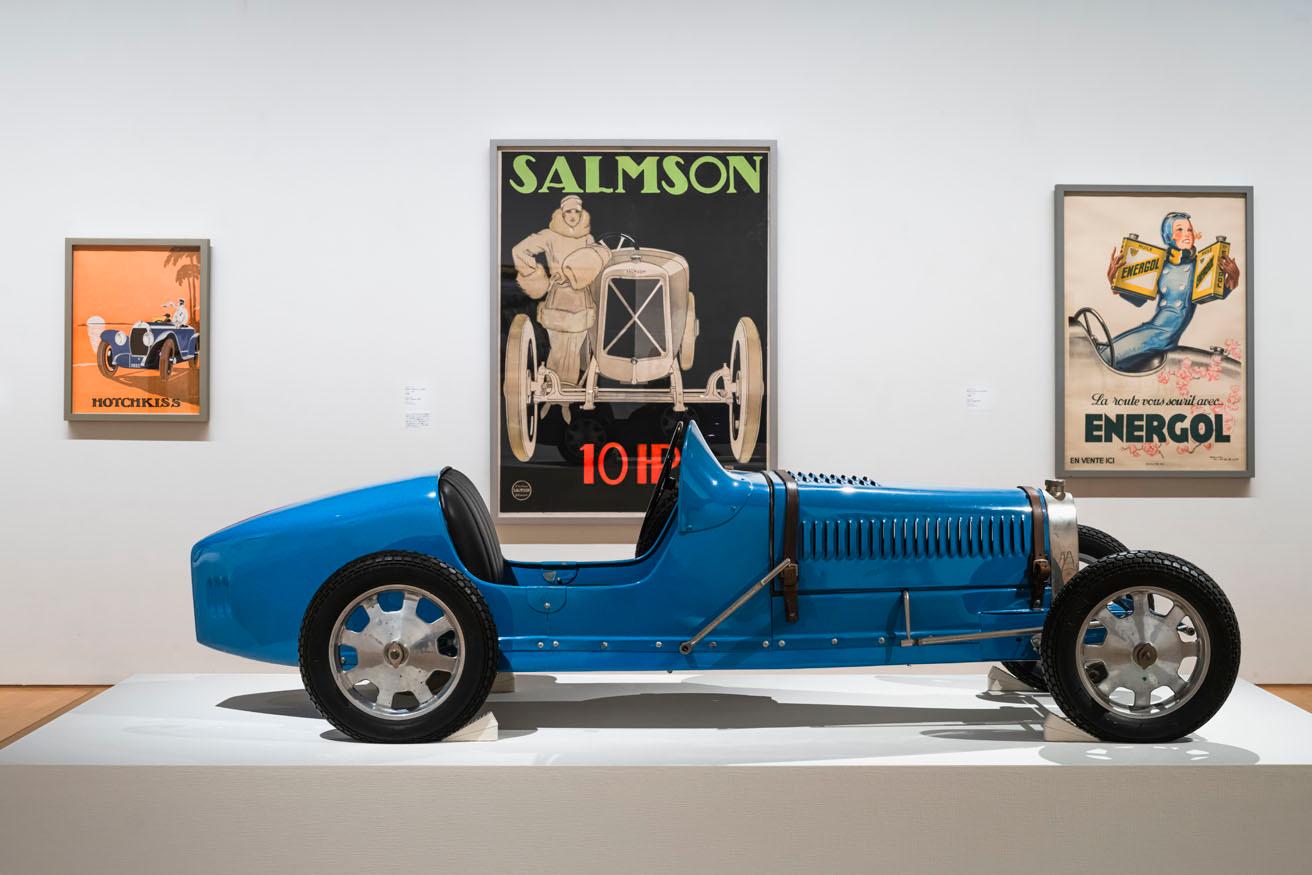「モダン・タイムス・イン・パリ 1925 ― 機械時代のアートとデザイン」展示風景「第1章　機械と人間：近代性のユートピア」より。手前は《ブガッティ　タイプ52（ベイビー）》（1920年代後半〜30年代初期・ブガッティ社、トヨタ博物館蔵）。実物の1/2の子ども向けの電気自動車。機能だけでなくエレガントさを追求したフォルム。　photo_Ooki JINGU